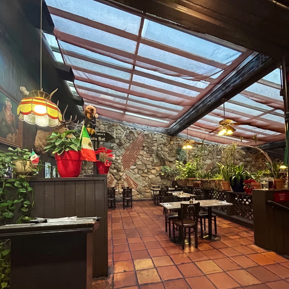 Sunlit restaurant atrium with tiled floors, stone walls, tropical plants, dining tables, and whimsical animal decorations.